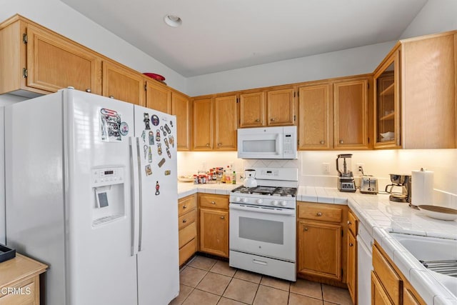 kitchen with tasteful backsplash, light tile patterned flooring, tile counters, and white appliances