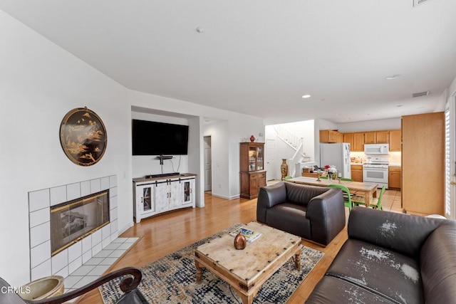 living room featuring a tiled fireplace and light wood-type flooring