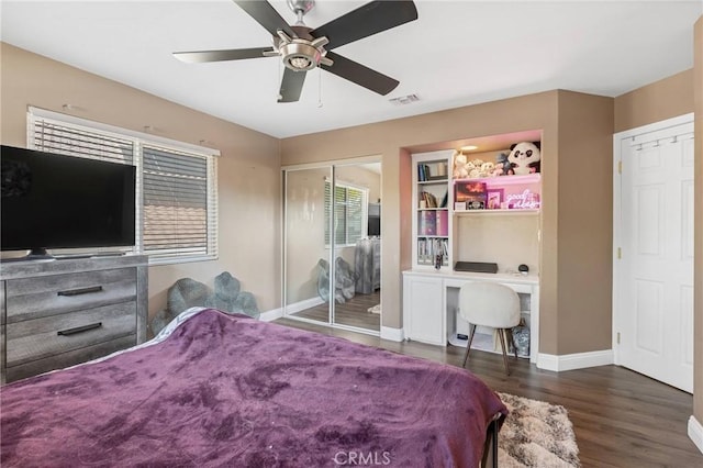 bedroom featuring built in desk, dark wood-type flooring, a closet, and ceiling fan