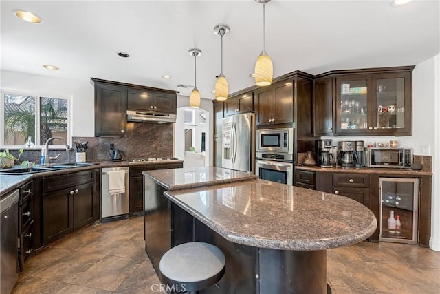 kitchen with a kitchen island, pendant lighting, dark stone counters, stainless steel appliances, and dark brown cabinets