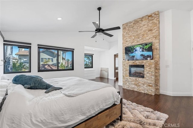 bedroom with ceiling fan, a stone fireplace, dark hardwood / wood-style flooring, and vaulted ceiling