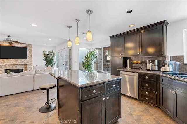 kitchen featuring a stone fireplace, dishwasher, a center island, dark brown cabinetry, and decorative light fixtures