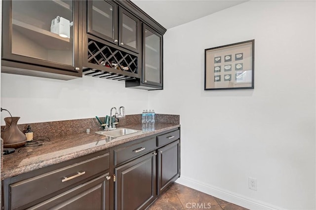 bar with light stone counters, sink, and dark brown cabinetry