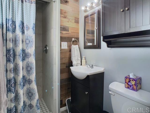 bathroom featuring toilet, vanity, wooden walls, and curtained shower