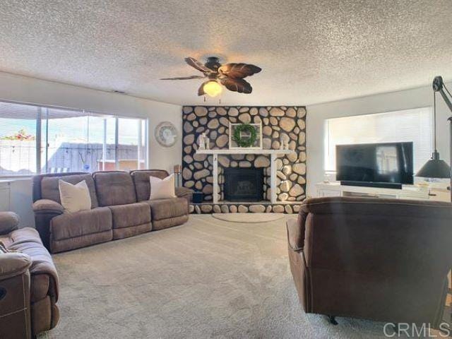 living room with a stone fireplace, a textured ceiling, ceiling fan, and carpet