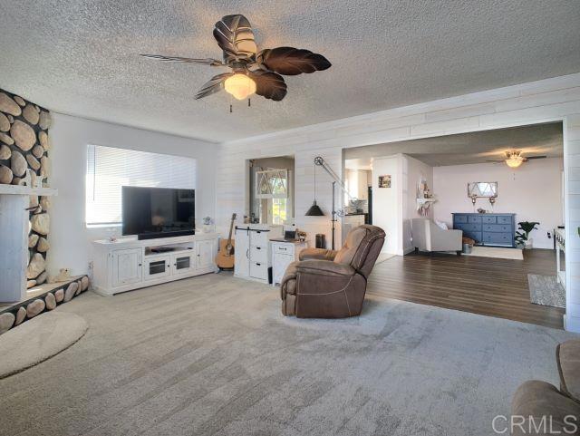 living room with ceiling fan, carpet flooring, a textured ceiling, and a fireplace