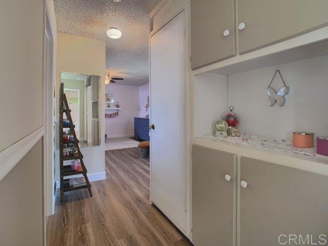 hall featuring baseboards, a textured ceiling, and wood finished floors