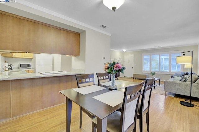 dining room with ornamental molding, sink, and light wood-type flooring