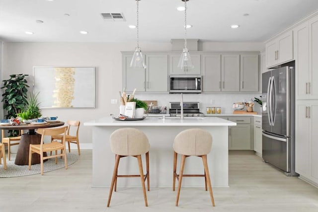 kitchen with a breakfast bar, sink, pendant lighting, stainless steel appliances, and a kitchen island with sink