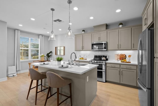 kitchen featuring sink, light hardwood / wood-style flooring, appliances with stainless steel finishes, an island with sink, and pendant lighting