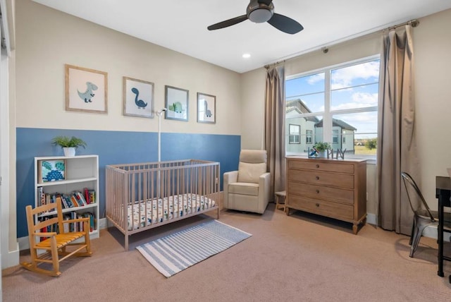 carpeted bedroom with a crib and ceiling fan