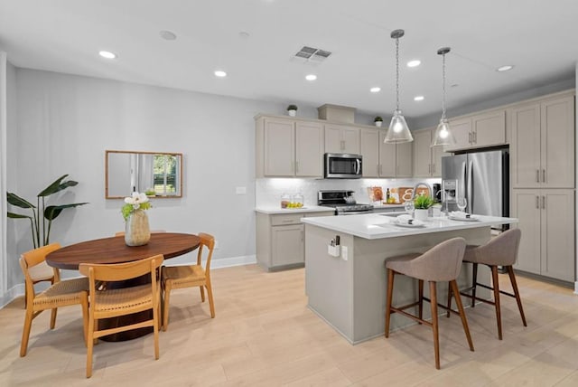 kitchen featuring stainless steel appliances, pendant lighting, gray cabinets, and a center island with sink