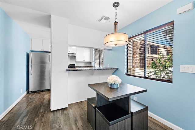 kitchen with pendant lighting, white cabinets, stainless steel fridge, dark stone counters, and dark wood-type flooring