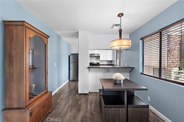 kitchen with stainless steel refrigerator, backsplash, dark hardwood / wood-style flooring, white cabinets, and hanging light fixtures