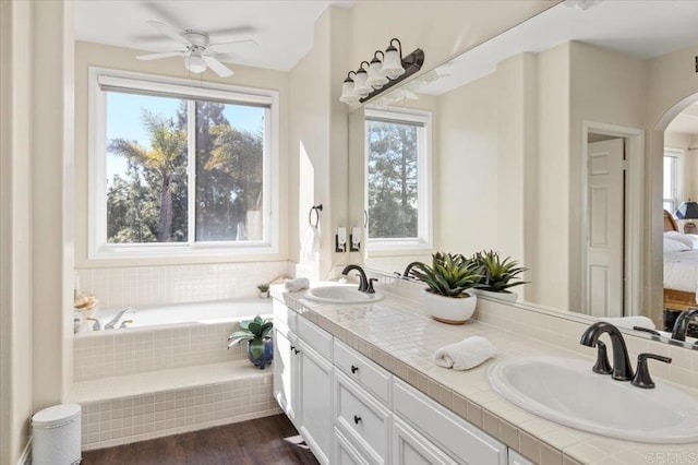 bathroom featuring hardwood / wood-style flooring, ceiling fan, vanity, and tiled tub