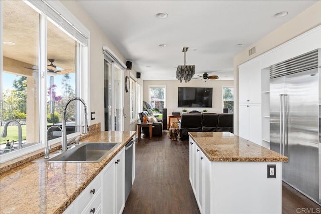 kitchen featuring sink, white cabinetry, stainless steel appliances, a center island, and light stone countertops