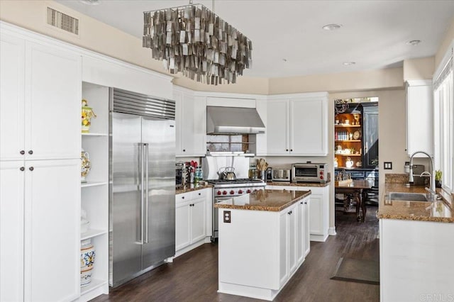 kitchen featuring wall chimney exhaust hood, sink, white cabinetry, premium appliances, and dark stone counters