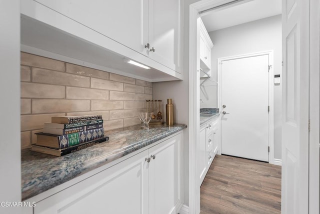 bar with tasteful backsplash, white cabinetry, light wood-type flooring, and dark stone counters