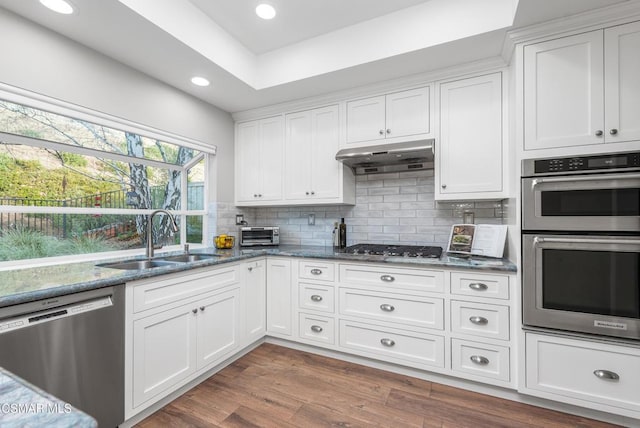 kitchen with sink, appliances with stainless steel finishes, dark stone countertops, white cabinets, and decorative backsplash