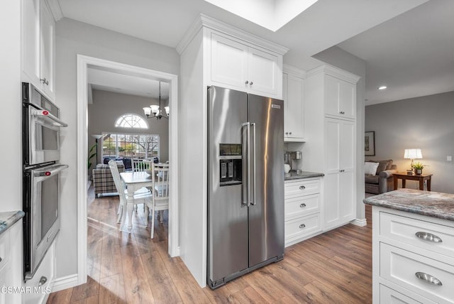 kitchen featuring white cabinetry, appliances with stainless steel finishes, wood-type flooring, and a notable chandelier