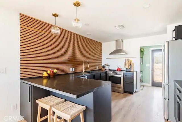 kitchen featuring a breakfast bar, hanging light fixtures, kitchen peninsula, wall chimney range hood, and stainless steel range oven