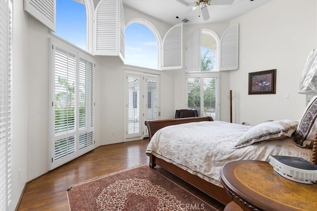 bedroom featuring dark hardwood / wood-style flooring, access to outside, ceiling fan, and a high ceiling