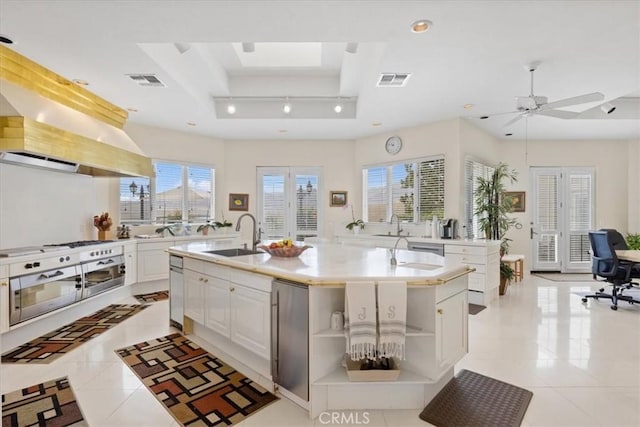 kitchen featuring white cabinetry, sink, a kitchen island with sink, light tile patterned floors, and a tray ceiling