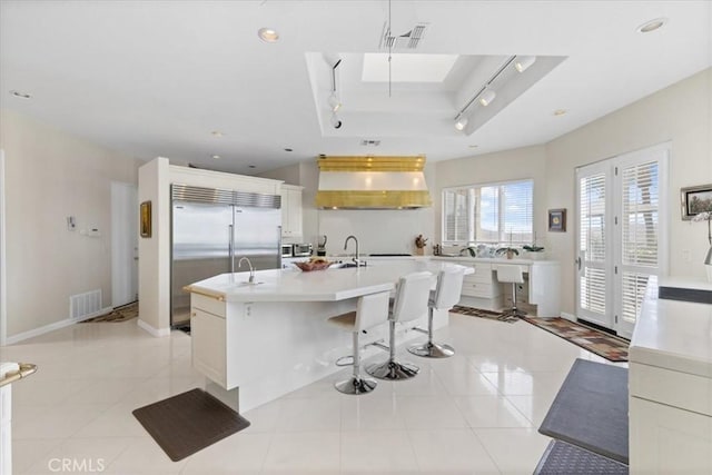 kitchen with wall chimney range hood, light tile patterned floors, a kitchen bar, and a center island with sink