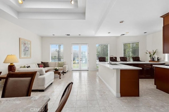 kitchen with french doors, sink, light tile patterned floors, a raised ceiling, and an island with sink