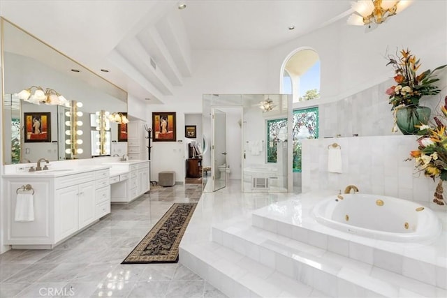 bathroom with tiled tub, vanity, a high ceiling, and toilet