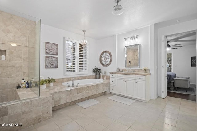 bathroom with vanity, ceiling fan with notable chandelier, tile patterned floors, and tiled bath