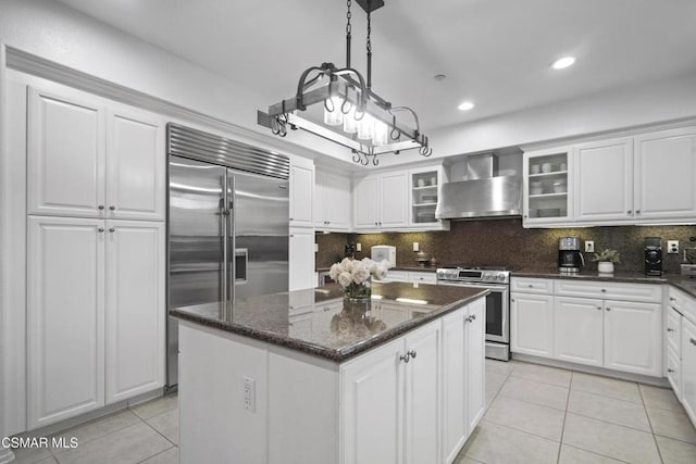 kitchen featuring wall chimney range hood, white cabinetry, stainless steel appliances, a center island, and decorative light fixtures