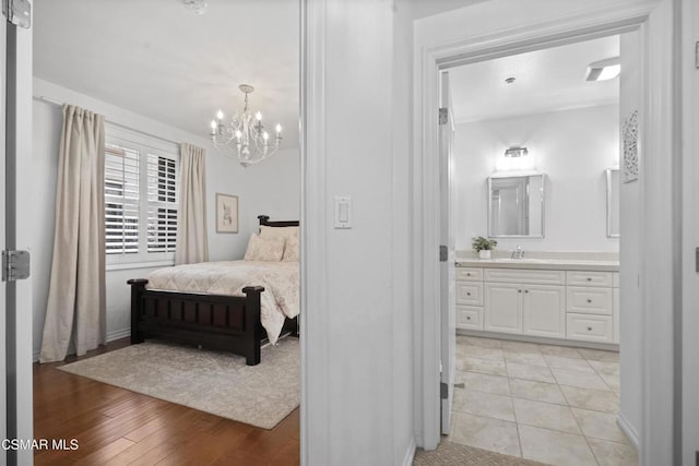 bedroom with connected bathroom, sink, a chandelier, and light wood-type flooring