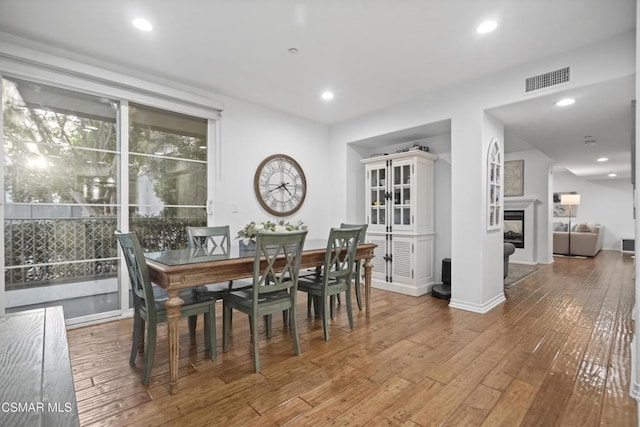 dining space with hardwood / wood-style flooring and a multi sided fireplace