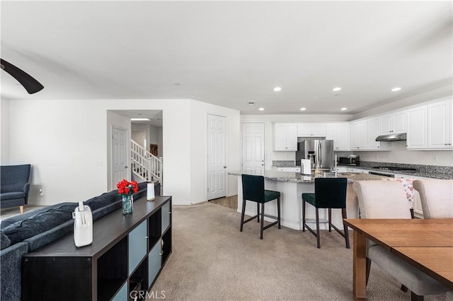 kitchen featuring a kitchen bar, light carpet, appliances with stainless steel finishes, light stone countertops, and white cabinets