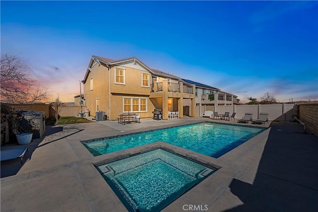 pool at dusk with an in ground hot tub and a patio area