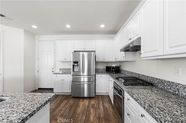 kitchen with appliances with stainless steel finishes, dark wood-type flooring, dark stone countertops, and white cabinets