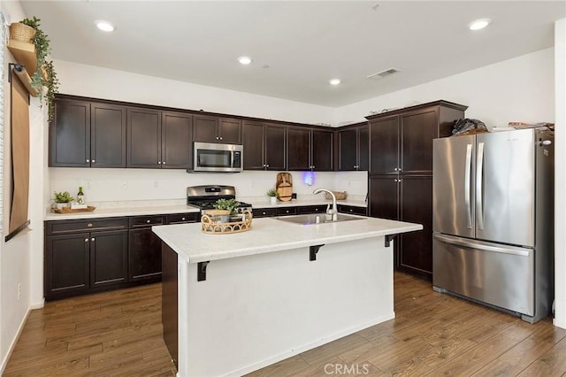 kitchen with sink, dark wood-type flooring, stainless steel appliances, and a center island with sink