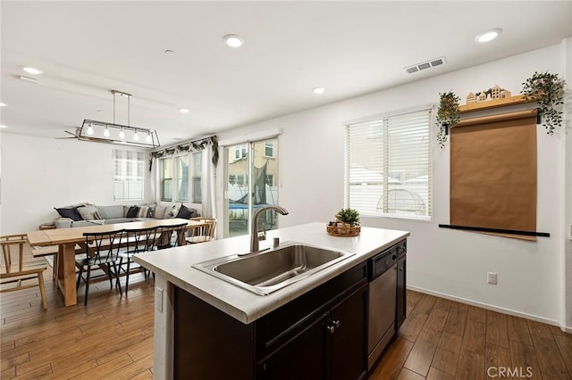 kitchen with decorative light fixtures, dishwasher, sink, dark hardwood / wood-style flooring, and a center island with sink