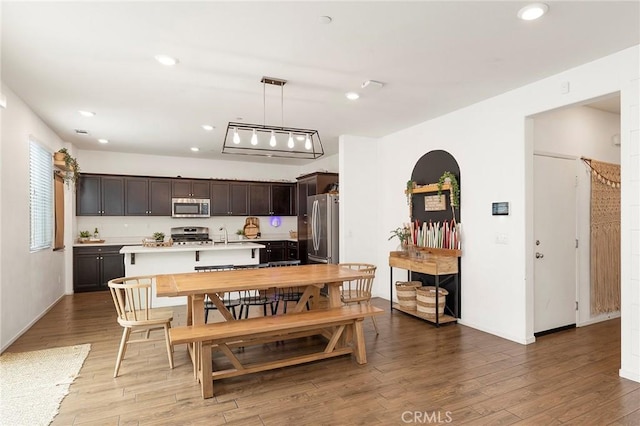 kitchen featuring decorative light fixtures, dark brown cabinets, wood-type flooring, and appliances with stainless steel finishes