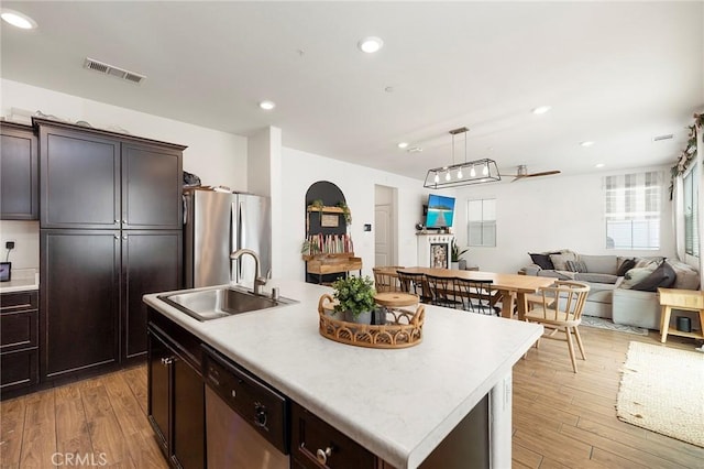 kitchen featuring sink, dark brown cabinets, light wood-type flooring, appliances with stainless steel finishes, and a kitchen island with sink