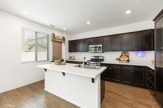 kitchen with dark brown cabinets, stainless steel appliances, a breakfast bar area, and a center island with sink