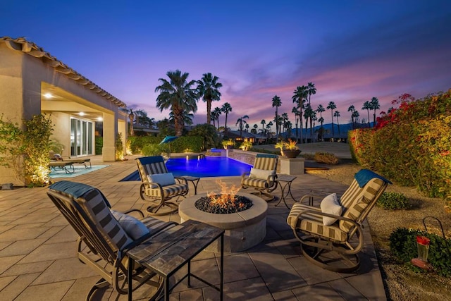 patio terrace at dusk featuring a fire pit and pool water feature