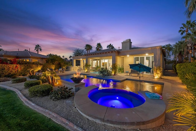 pool at dusk featuring an in ground hot tub, a patio area, and a fire pit