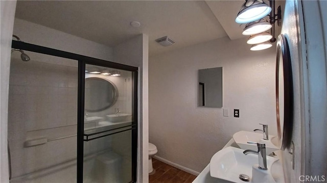 bathroom with a shower with door, dual sinks, and toilet