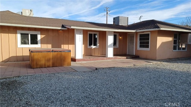 rear view of property with cooling unit, a hot tub, and a patio