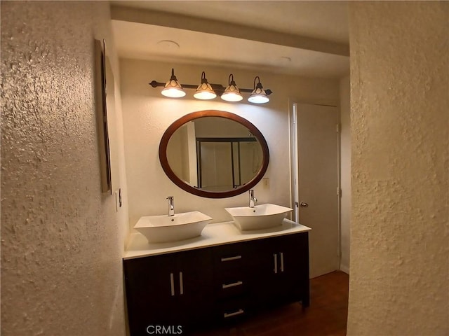 full bath with double vanity, a sink, and a textured wall