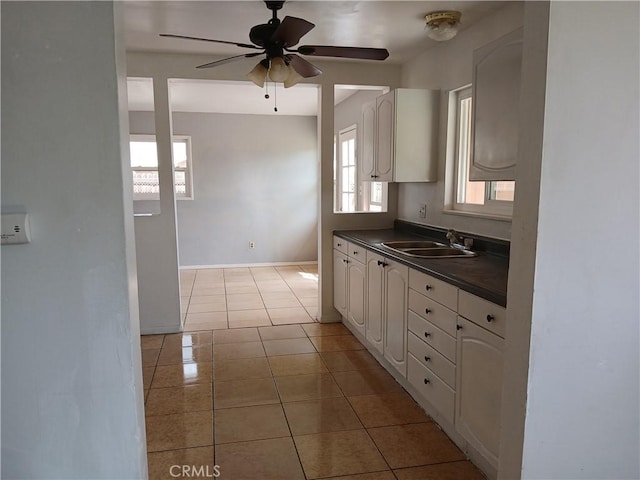 kitchen with ceiling fan, light tile patterned flooring, a sink, white cabinetry, and dark countertops