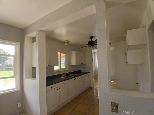 kitchen with dark countertops, white cabinets, light tile patterned flooring, a sink, and ceiling fan