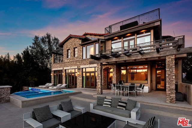 back house at dusk with a swimming pool with hot tub, a patio area, outdoor lounge area, and a balcony